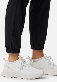 White athletic shoes with mesh detailing and laces, paired with black tapered joggers featuring elastic cuffs at the ankle.