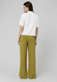 Blouse blanche à manches courtes avec un col, associée à un pantalon large taille haute en olive. Tissu léger et coupe décontractée.