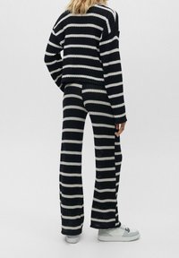 Ensemble tricoté en noir et blanc avec un pull et un pantalon, présentant une coupe décontractée, une texture côtelée et un design à jambes larges. Agrémenté d'un pli décontracté.