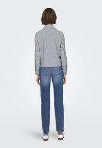 Jeans in denim blu, design a gamba dritta, lavaggio sbiadito, abbinati a una camicia button-up a righe grigie e bianche con maniche arrotolate.