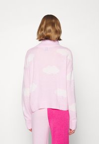 Pastellrosa Pullover mit weißen Wolkenmustern, geripptem Saum und Bündchen, lockerer Schnitt, kombiniert mit pinken und hellpinken Hosen.