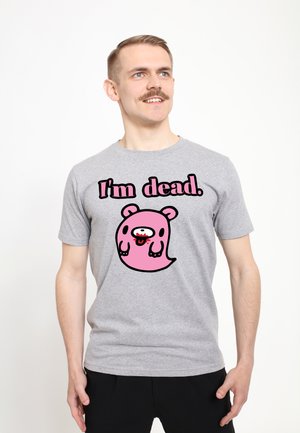 Uomo con capelli corti e baffi, indossa una maglietta grigia con un fantasma rosa in stile cartone animato e la scritta "I'm dead." guarda leggermente verso l'alto sorridendo.