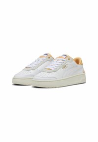 Sneakers bianchi con tomaia in pelle liscia, dettagli beige, punta arrotondata e suola in gomma spessa. Presentano un design con lacci e perforazioni.