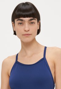 Mørkeblå ærmeløs top med tynde stropper, i et glat, elastisk stof og en rundet halsudskæring. Enkel, minimalistisk design.