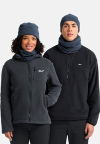 Zwei Personen tragen Fleecejacken in Dunkelgrau und Schwarz; beide haben passende Strickmützen und Schlauchschals in einem ähnlichen dunklen Farbton.