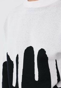 Suéter en blanco y negro con un diseño de pintura goteante, cuello redondo acanalado y un patrón de punto texturizado en toda su superficie.