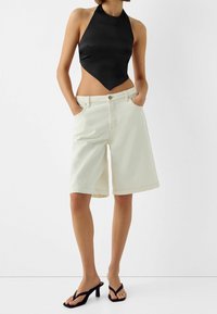 Svart halterneck bodysuit kombinerat med ljust beige denimshorts i knä-längd. Har framfickor och rak skärning, med svarta klacksandaler.