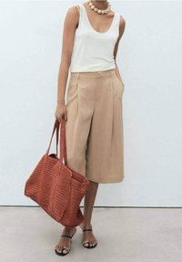 Pantalon beige à jambes larges, débardeur blanc, sac rouge en tricot, et sandales noires avec des accents métalliques. Tissu lisse et coupe décontractée.