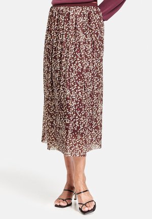 Vrouw draagt een bruine midi-rok met een wit bladerenpatroon, gecombineerd met zwarte sandalen met hoge hakken en een paarse top.