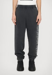 Graue Sweatpants aus weichem Baumwollmaterial, mit gerippten Bündchen und einem gemusterten Logo-Print entlang der linken Seite. Lockere Passform mit elastischem Bund.