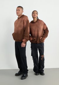 Hanorace cu un gradient maro, dotate cu buzunare tip kangaroo, purtate cu pantaloni distresați negri și încălțări negre. Finish mat, croială lejeră.