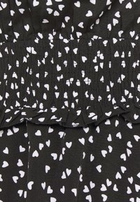 Svart tyg med vitt hjärtmönster, med samlad textur upptill och en volangkant. Lätt och smidigt material.