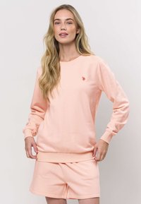 Svetle růžová mikina s žebrovanými man žetami a lemem, na hrudi malým vyšívaným logem. Doplněna o odpovídající šortky.