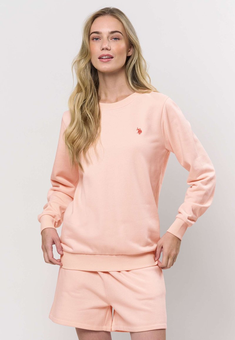 Svetle růžová mikina s žebrovanými manžetami a lemem, na hrudi malým vyšívaným logem. Doplněna o odpovídající šortky.