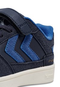 Blå och mörkgrå sneaker med överdel i mocka och läder, kardborreband och kontrasterande zigzagdetaljer. Vit gummisula.