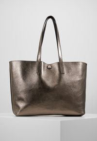 Sac cabas en cuir texturé bronze métallique avec deux longues poignées et un petit bouton rond au centre en haut.