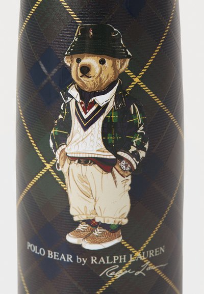 Meda teddy s kapom, kariranom košuljom, bijelim pletenim džemperom, bež hlačama i tenisicama na tamnoj kariranoj pozadini s natpisom "POLO BEAR by RALPH LAUREN."