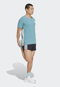 Modrá športová tričko s bodkovanou textúrou a bielymi akcentmi, kombinované s čiernymi šortkami s bielymi pruhmi a bielymi športovými topánkami.