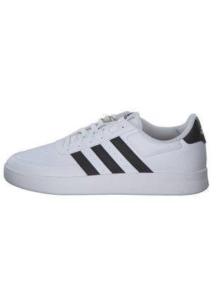 Biały niski sneaker z czarnymi paskami, białymi sznurówkami i czarną pętelką na pięcie, widziany z boku na białym tle.