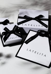 Tre hvide gavekasser med sort bånd, der viser logoet "LATELITA." Den største kasse har en sort kant; båndene har tekstdetaljer.