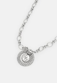 Zilveren ketting met een spiraalvormige hanger versierd met rhinestones en een centraal logo-detail, die een gepolijste metaalafwerking laat zien.