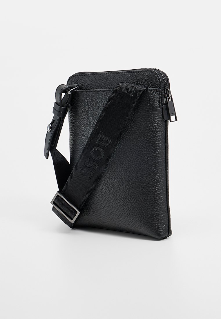 Sac bandoulière en cuir noir avec une finition texturée, fermeture zippée, bandoulière réglable arborant un logo, et une forme rectangulaire élégante.