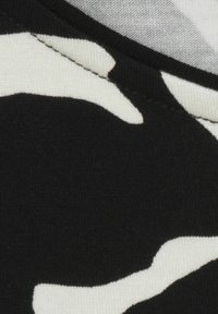 Schwarzer Stoff mit einem weißen Camouflage-Muster; weiche Textur mit sichtbaren Nähten. Das Design zeigt fließende, unregelmäßige Formen.