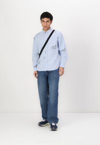 Light blue button-up shirt with black line patterns, paired with blue jeans and navy sneakers; features a crossbody bag for functionality.