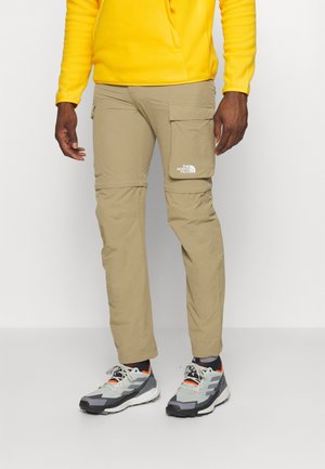 Homme portant un pantalon cargo kaki avec le logo The North Face et des chaussures de sport grises avec des semelles blanches et des accents orange.