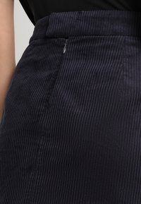 Marineblauwe corduroy rok met een gestructureerd, ribbelachtig oppervlak. Beschikt over een aansluitende taille en een discrete zijrits voor sluiting.