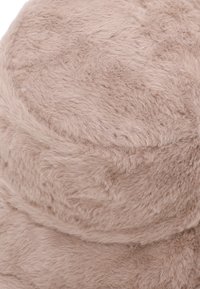 Cuscino in finta pelliccia di un morbido beige, a forma rotonda con una texture soffice e un delicato luccichio, caratterizzato da cuciture ornate per un ulteriore dettaglio.