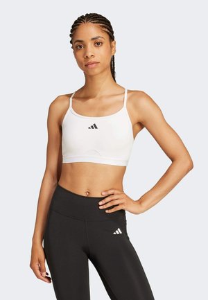 White sports bra with thin straps and a round neckline, featuring a black Adidas logo. Paired with high-waisted black leggings.