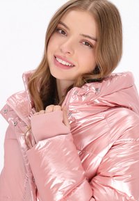 Rózsaszín fémes puf jacket kapucnival, patentgombokkal és elasztikus mandzsettákkal, fényes textúrával és steppelt kialakítással.