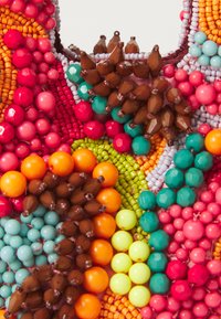 Perletilbehør med livlige farger som oransje, rosa, grønn og turkis. Tett arrangert med perler i ulike størrelser og former.