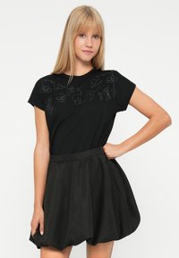 Black t-shirt with floral embroidery on the neckline, paired with a black, textured, balloon-style skirt with a gathered waistband.