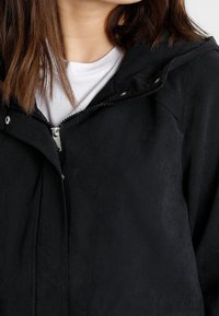 Giacca nera con un tessuto liscio e textured, con chiusura frontale a zip e cappuccio; include dettagli in metallo argentato sulla zip.