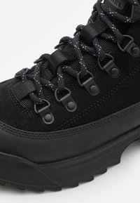 Czarne buty trekkingowe z cholewką z zamszu i teksturowanej siateczki, z czarnymi dodatkami, okrągłymi sznurowadłami oraz trwałą gumową podeszwą o wyraźnym bieżniku.