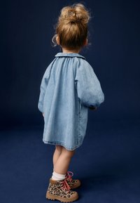 Denimkleid mit Puffärmeln, Kragen und gerafftem Rückendetail, kombiniert mit Leopardenmuster-Stiefeln mit rosa Schnürsenkeln und weißen Socken.