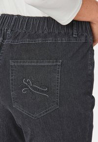 Pantalon en denim gris foncé avec une taille élastique et une poche arrière ornée d'un design brodé décoratif en fil clair.