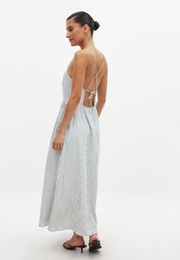 Robe maxi rayée en bleu clair et blanc, avec une découpe dans le dos et des bretelles croisées. Tissu lisse avec une silhouette fluide.
