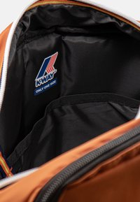 Zaino K-Way con esterno arancione e interno nero. Presenta una patch con logo e una chiusura con cerniera. L'interno include una tasca in rete.