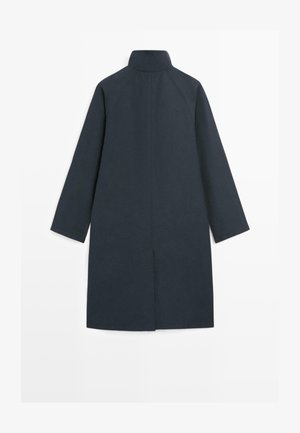 Długi ciemnogranatowy płaszcz z wysokim kołnierzem i długimi rękawami, prosty krój i detal rozcięcia z tyłu.