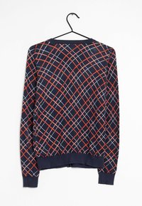 Granatowy sweter z geometridosisowym czerwono-białym wzorem w kratkę, okrągłym dekoltem oraz prążkowanymi mankietami i dołem; powieszony na czarnym wieszaku.