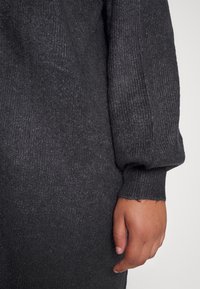 Dark grey knitted dress with ribbed texture, balloon sleeves, and frayed hem. A hand is visible on the sleeve for scale.