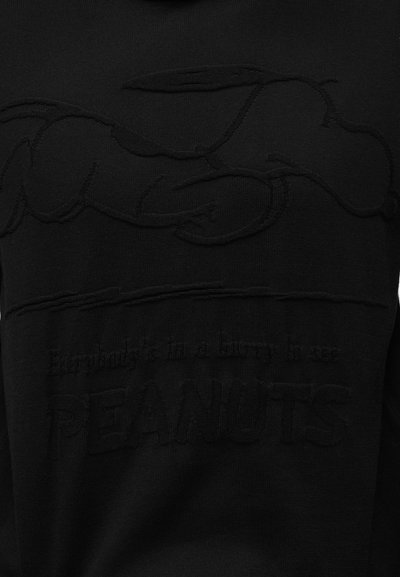 Μαύρο ύφασμα με ανάγλυφη εικόνα του Snoopy να ξαπλώνει από πάνω και κείμενο που λέει "Όλοι διασκεδάζουν διασκεδάζοντας με τους PEANUTS."