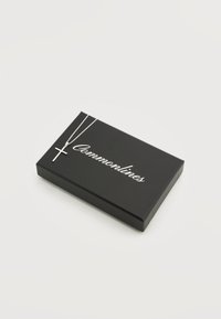 Κολιέ με ασημένιο σταυρό σε μαύρο κουτί με την επιγραφή «Commonlines» σε απλό ανοιχτό φόντο.