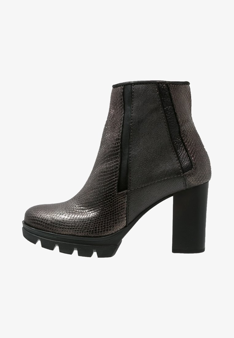 Bottine noire à talon haut en cuir texturé, semelle épaisse à crampons, panneaux latéraux élastiques et talon bloc sur fond blanc.