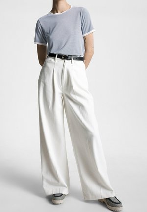 Chemise à manches courtes rayée bleue et blanche, pantalon large blanc taille haute, ceinture noire et baskets grises avec des motifs texturés.