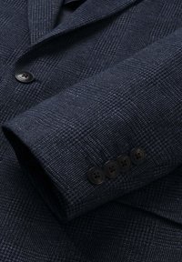 Tmavě modrý blejzr s jemným kostkovaným vzorem, s čtyřmi knoflíky na rukávech a jedním předním knoflíkem označeným "London".