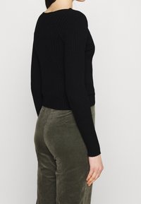 Svart ribbad stickad tröja med långa ärmar och figurnära design. Bärs tillsammans med olivgröna manchesterbyxor som har en strukturerad finish och avslappnad passform.